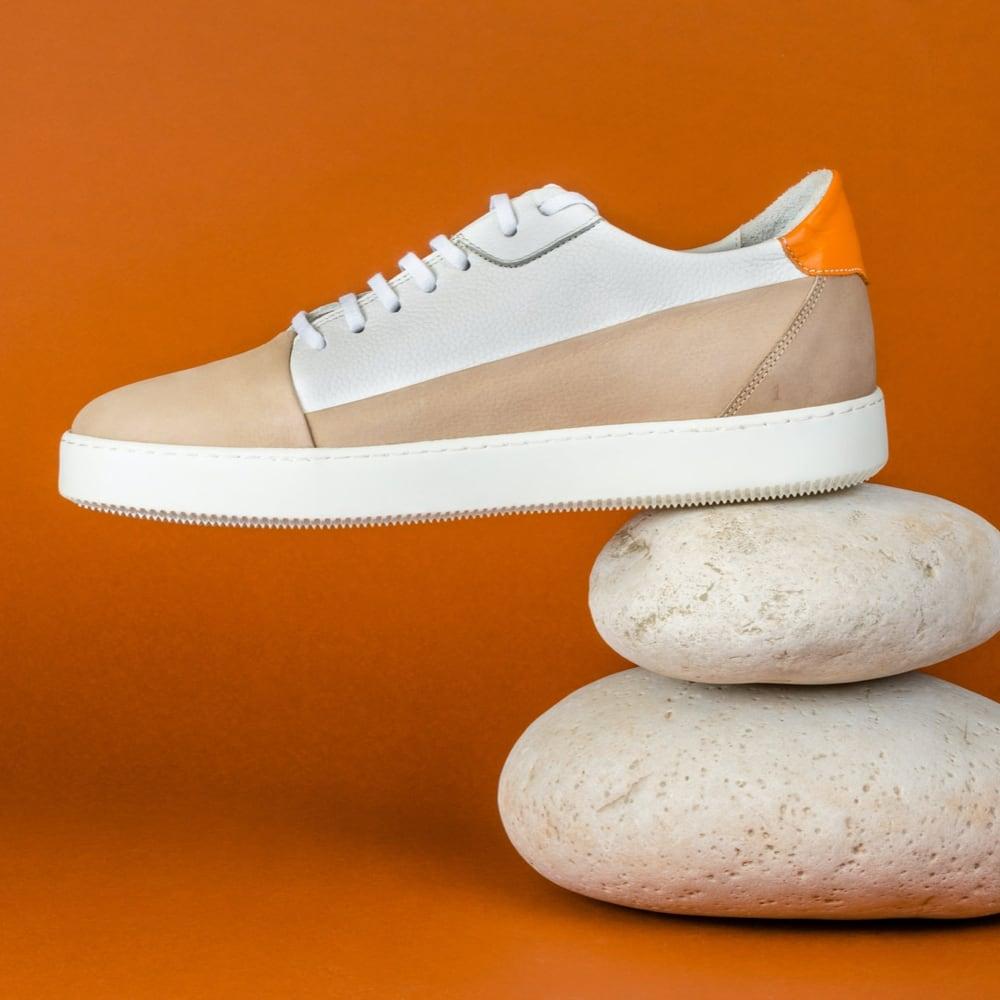 Profile shot of the product, white sneakers on orange background